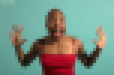 A bald black woman splaying her hands out to the sides and looking at the camera with an exuberant expression