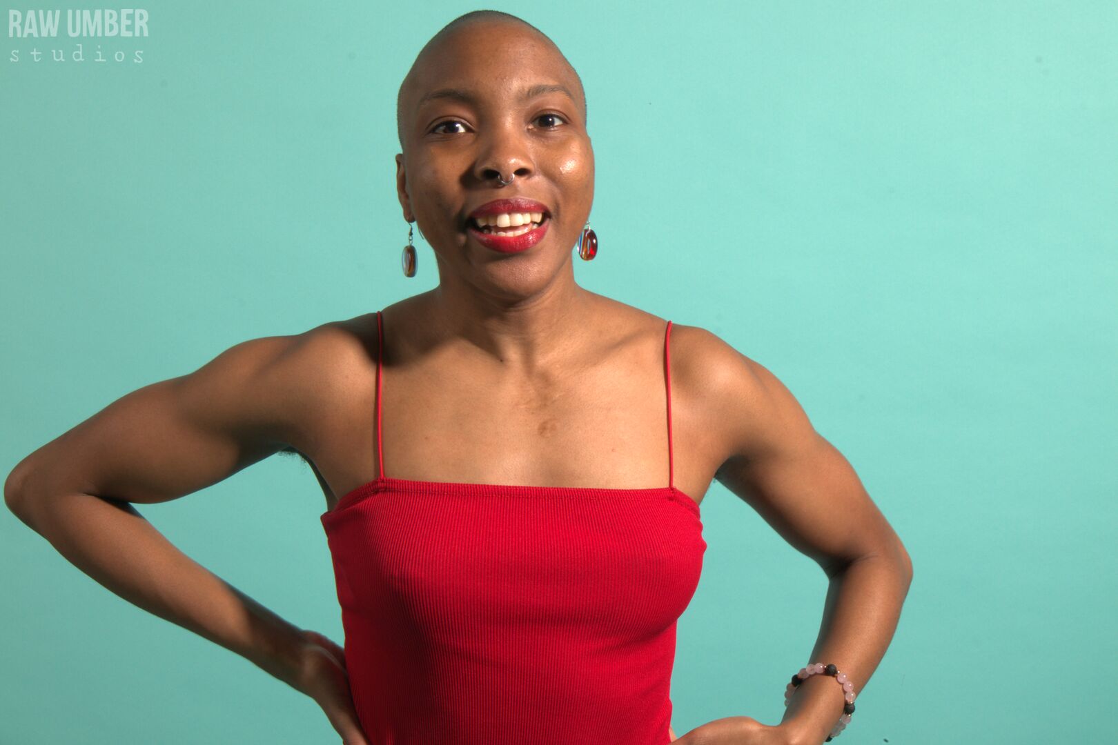 A bald black woman with her hands on her hips glancing to the left of the camera with a smile