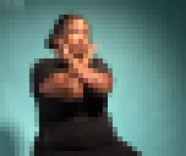 A three quarter profile of a young black woman with brown hair tied in a bun sitting with her arms crossed over her chest, the backs of her hands against her cheeks, looking upward with a neutral expression. 