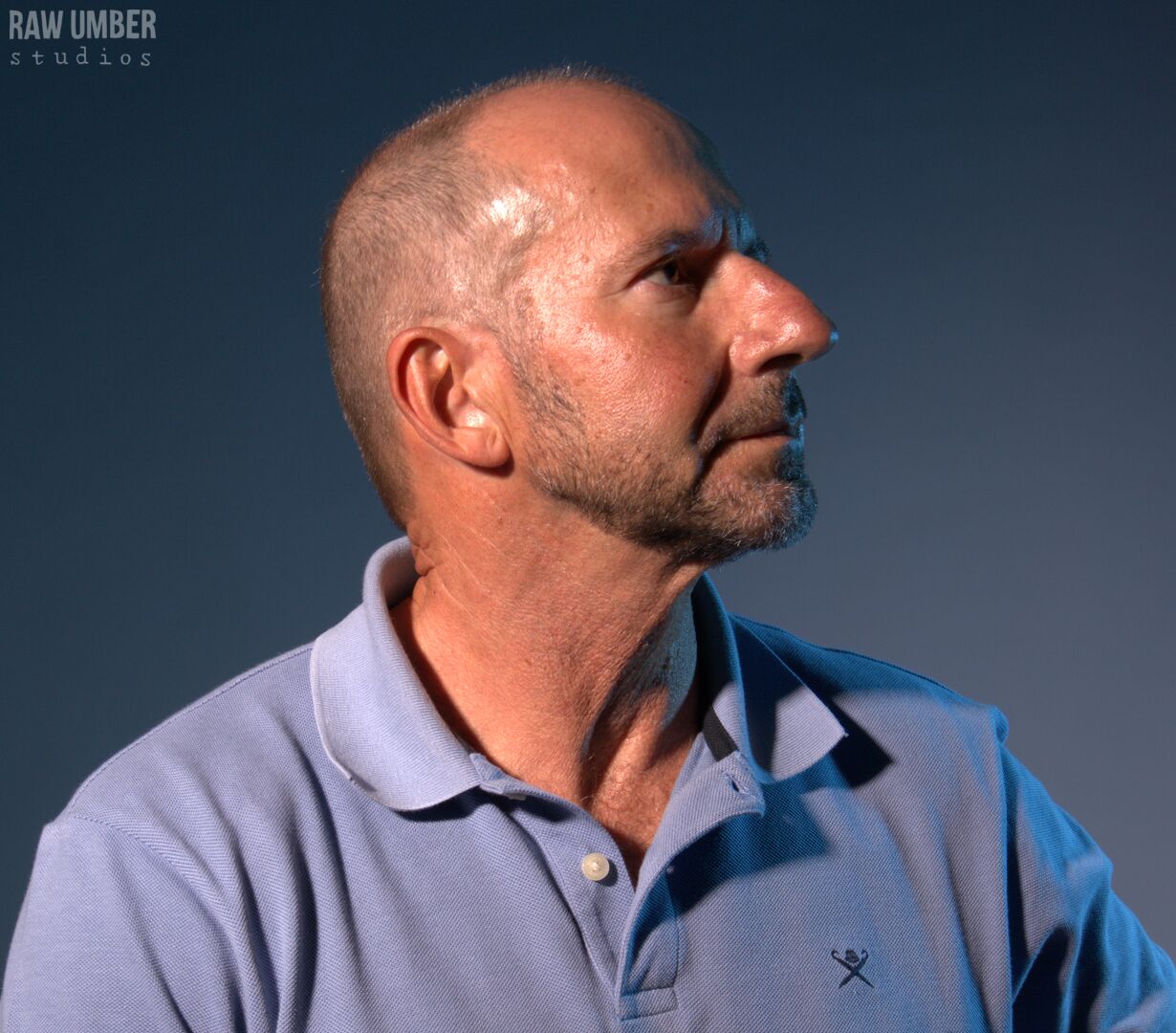 A profile of a bald white man with stubble and a neutral expression