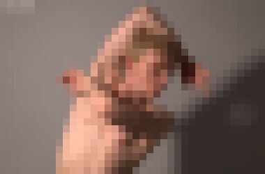 A nude white man with sort blond hair leaning to the right, his left arm across his chest and his right arm behind his head, with a meditative expression