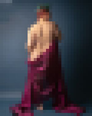 A back shot of a nude white woman with short, red and green two-toned hair and purple velvet draped aroudn their hips to the floor, looking to the right with a neutral expression
