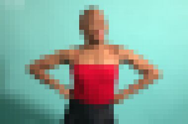A three quarter profile of a bald black woman with her hands on her hips glancing at the camera with a smile